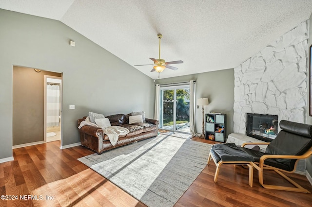 living room featuring hardwood / wood-style flooring, ceiling fan, a stone fireplace, and a textured ceiling