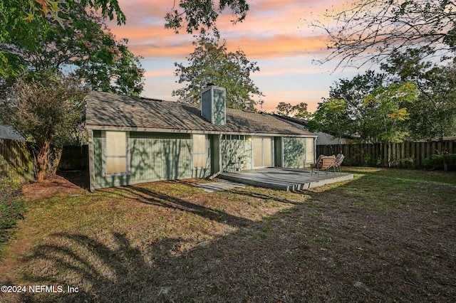 back house at dusk featuring a patio area and a lawn