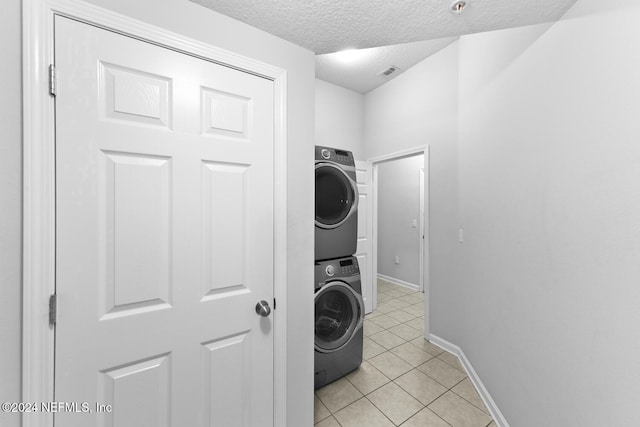 laundry area featuring stacked washer / drying machine, light tile patterned floors, and a textured ceiling