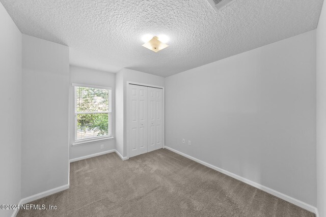 unfurnished bedroom with a closet, light colored carpet, and a textured ceiling