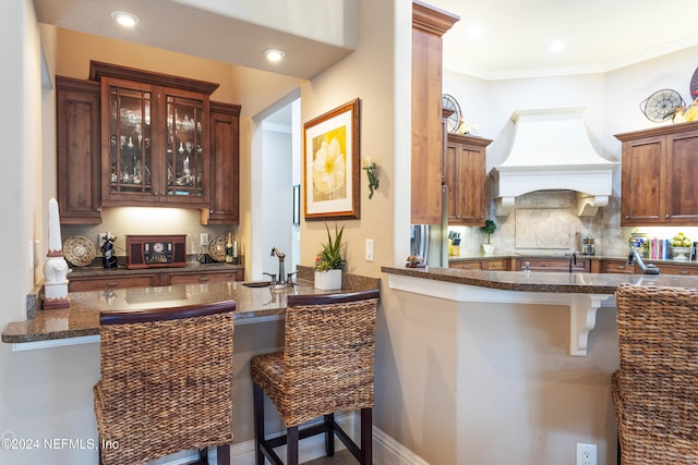 bar featuring dark stone counters, crown molding, sink, decorative backsplash, and custom range hood