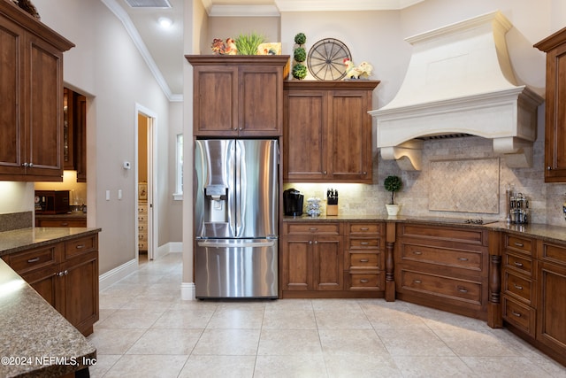 kitchen featuring stainless steel fridge, dark stone counters, custom range hood, and crown molding