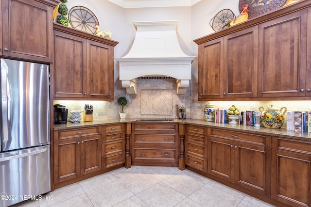 kitchen featuring decorative backsplash, custom range hood, crown molding, dark stone countertops, and stainless steel refrigerator