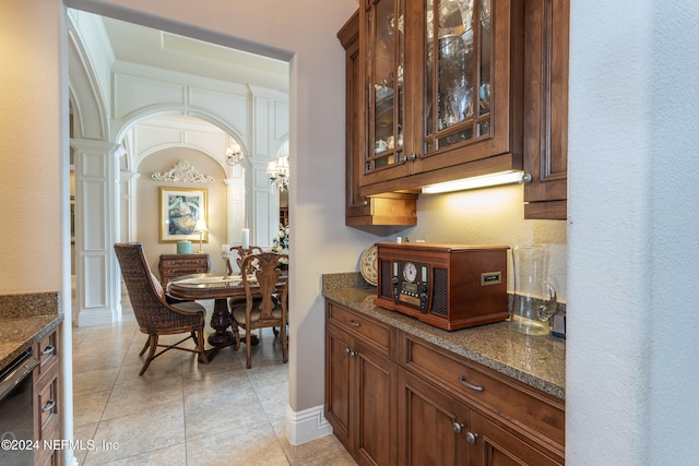 bar with ornate columns, stainless steel dishwasher, dark stone counters, light tile patterned floors, and ornamental molding