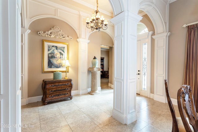 corridor with an inviting chandelier, decorative columns, a towering ceiling, light tile patterned floors, and ornamental molding