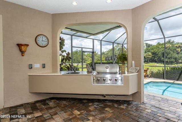 view of pool with area for grilling, sink, and glass enclosure