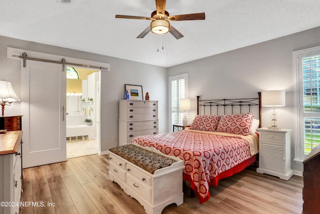 bedroom with a barn door, ensuite bathroom, light hardwood / wood-style flooring, and multiple windows