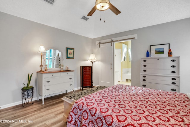 bedroom featuring ensuite bathroom, a textured ceiling, ceiling fan, a barn door, and light hardwood / wood-style flooring