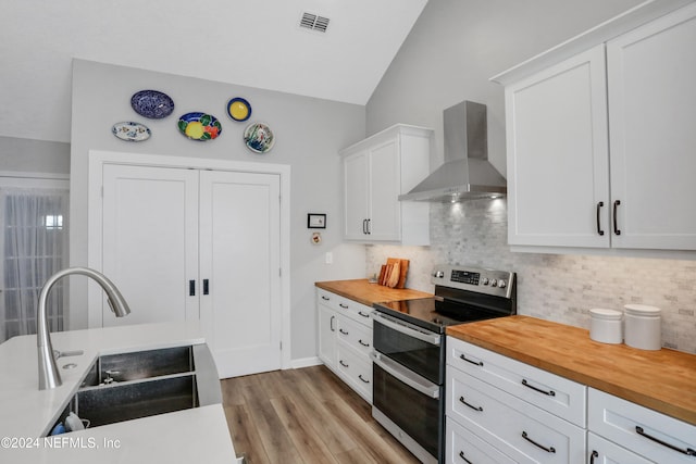 kitchen featuring lofted ceiling, white cabinets, wall chimney exhaust hood, stainless steel electric range oven, and butcher block counters