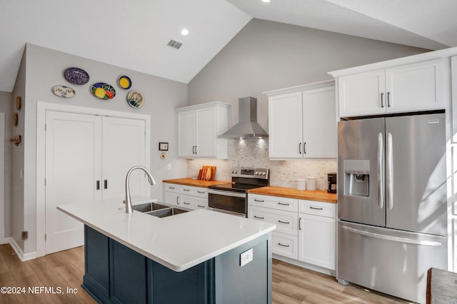 kitchen with sink, wall chimney exhaust hood, light hardwood / wood-style floors, a kitchen island with sink, and appliances with stainless steel finishes