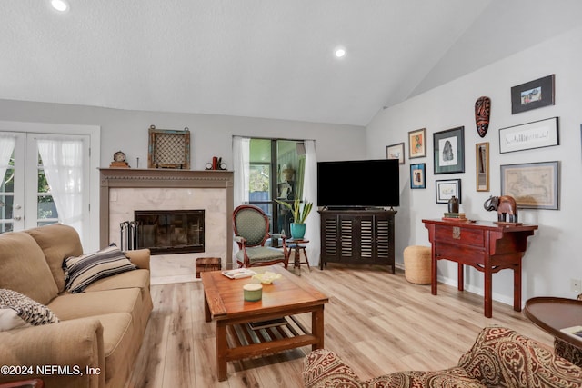 living room featuring a high end fireplace, french doors, light wood-type flooring, and lofted ceiling