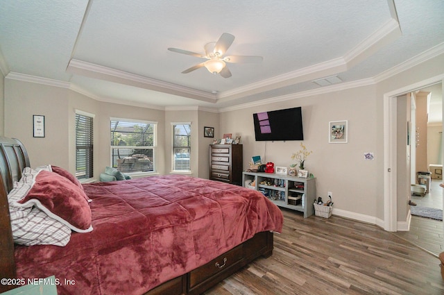 bedroom with visible vents, a raised ceiling, baseboards, and wood finished floors