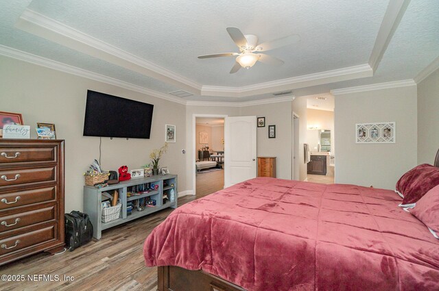 bedroom featuring a raised ceiling, crown molding, wood finished floors, and a textured ceiling