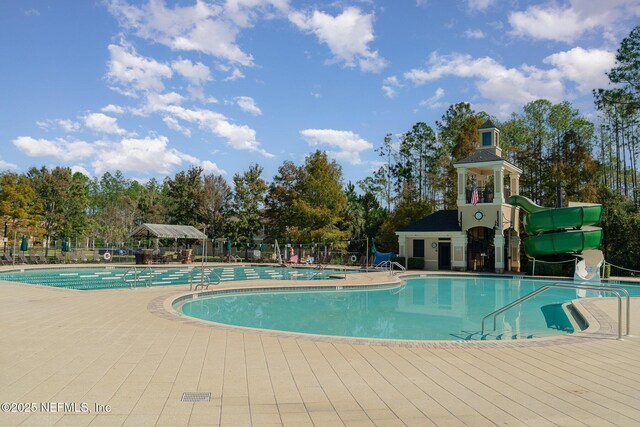 community pool with a patio area, a water slide, and fence