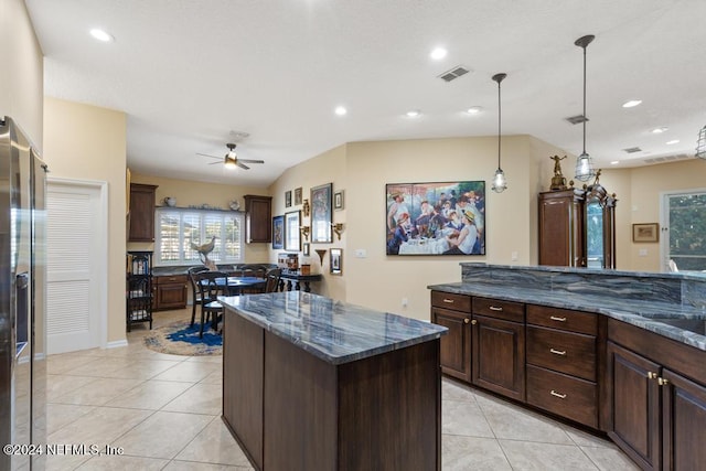 kitchen with dark stone countertops, a center island, light tile patterned floors, and decorative light fixtures