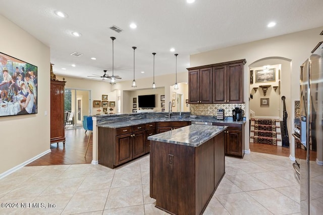 kitchen featuring ceiling fan, hanging light fixtures, kitchen peninsula, dark stone countertops, and light tile patterned floors