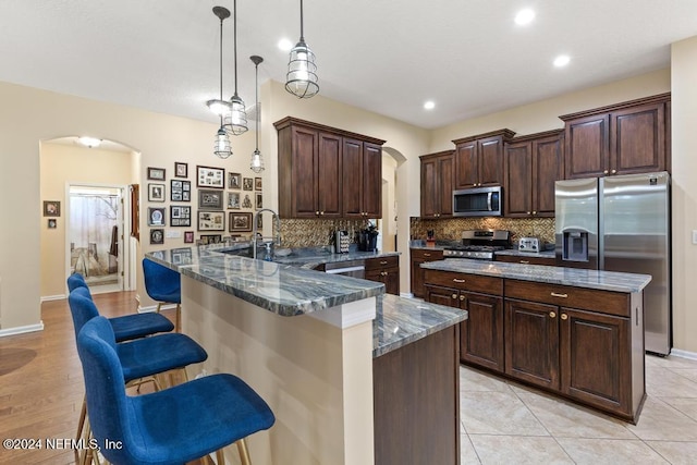 kitchen with kitchen peninsula, a breakfast bar, stainless steel appliances, dark stone countertops, and hanging light fixtures