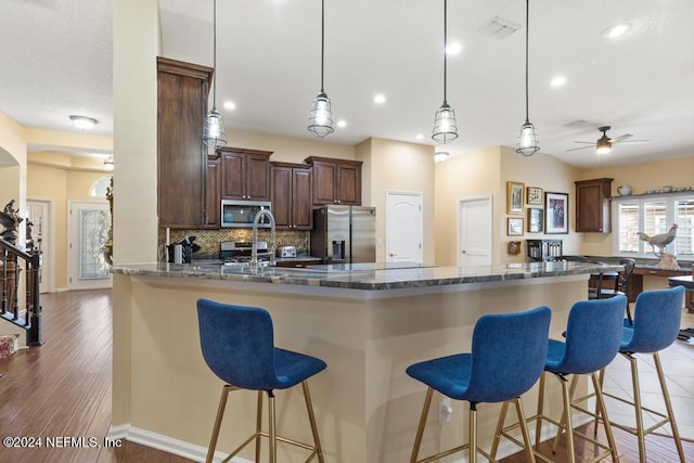 kitchen featuring ceiling fan, tasteful backsplash, dark stone countertops, a kitchen bar, and appliances with stainless steel finishes