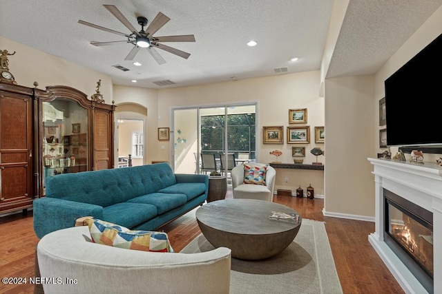 living room with ceiling fan, a textured ceiling, and dark wood-type flooring