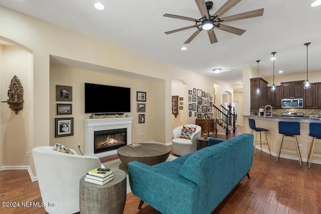 living room with ceiling fan, sink, and dark wood-type flooring