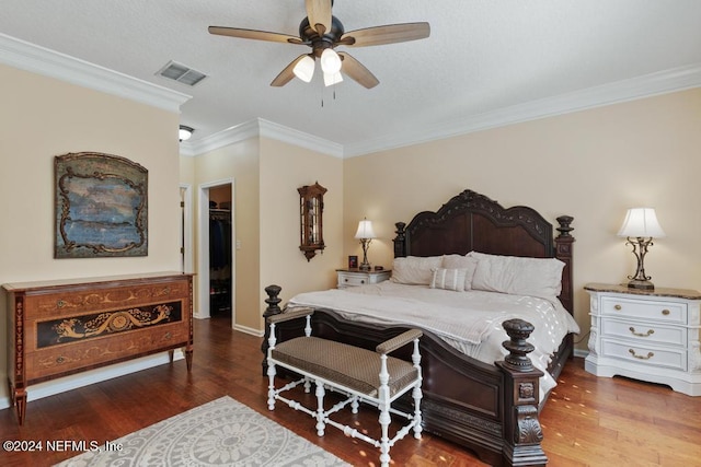 bedroom with a walk in closet, hardwood / wood-style flooring, ceiling fan, ornamental molding, and a closet