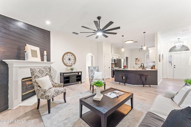 living room featuring ceiling fan, wood walls, light wood-type flooring, and sink