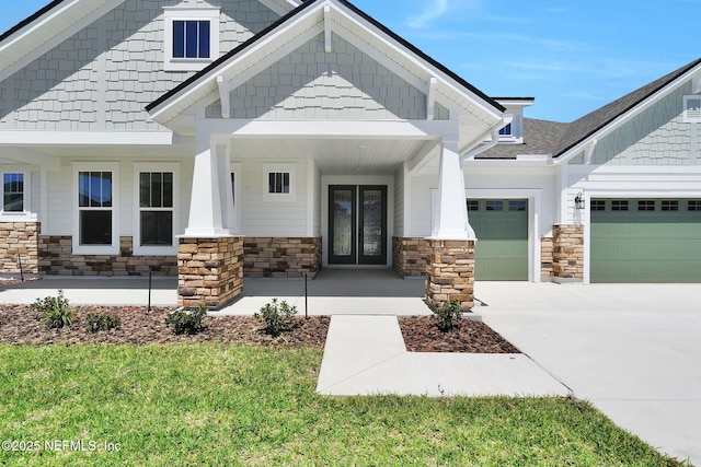 view of front of property featuring a garage, stone siding, french doors, driveway, and a porch