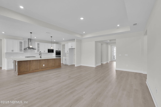 unfurnished living room featuring a sink, light wood-style flooring, recessed lighting, a tray ceiling, and baseboards