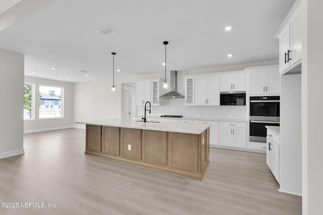 kitchen with wall chimney exhaust hood, stainless steel double oven, a sink, stovetop, and light wood-style flooring