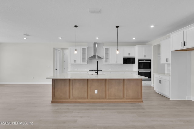 kitchen with wall chimney exhaust hood, stainless steel double oven, built in microwave, light countertops, and light wood-type flooring