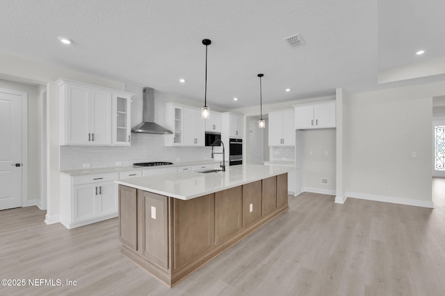 kitchen featuring wall chimney exhaust hood, light wood-type flooring, baseboards, decorative backsplash, and a sink