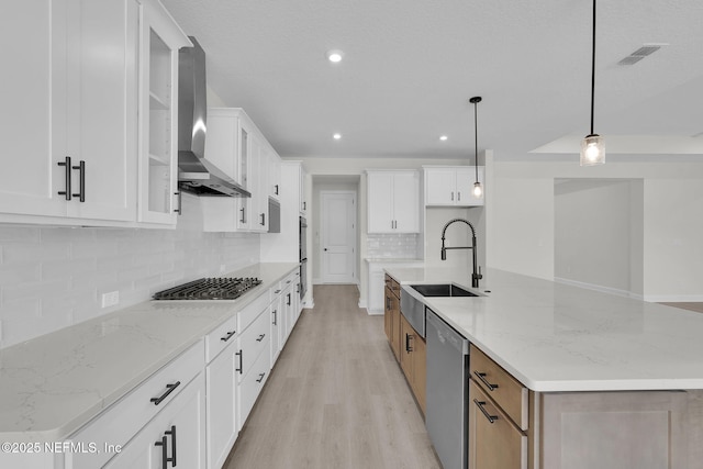 kitchen with wall chimney exhaust hood, appliances with stainless steel finishes, light wood finished floors, decorative backsplash, and a sink