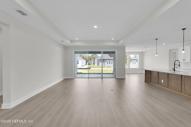 unfurnished living room featuring a sink, a tray ceiling, light wood-style floors, recessed lighting, and baseboards
