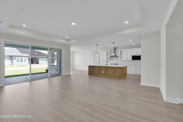 unfurnished living room featuring a tray ceiling, baseboards, light wood-style floors, a sink, and recessed lighting