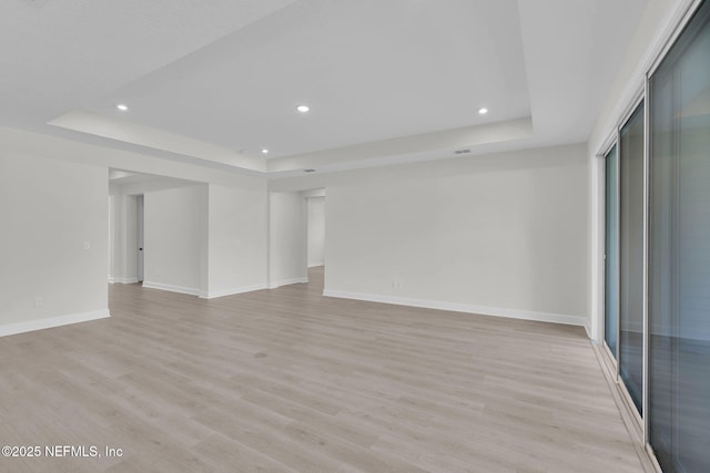 unfurnished living room with a tray ceiling, recessed lighting, light wood-type flooring, and baseboards