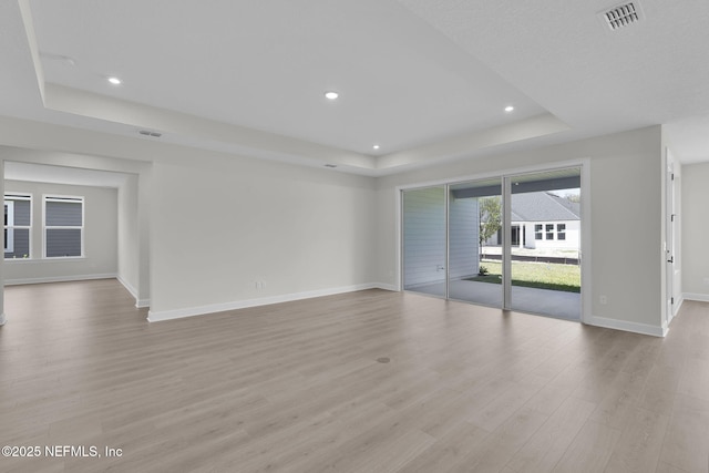 unfurnished room with a tray ceiling, baseboards, light wood finished floors, and recessed lighting