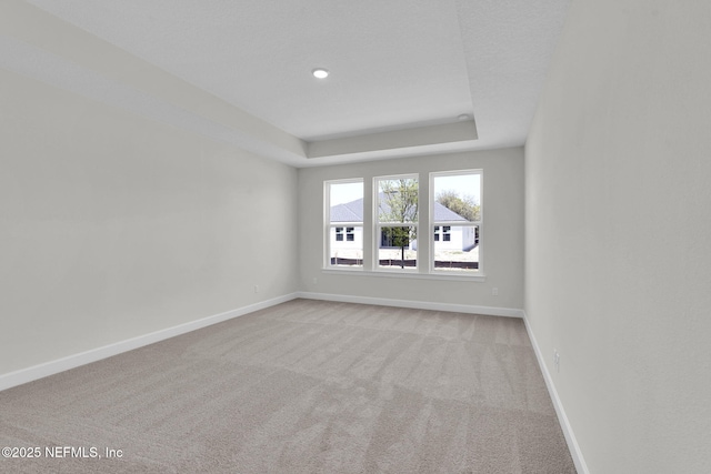 spare room with light colored carpet, baseboards, and a raised ceiling