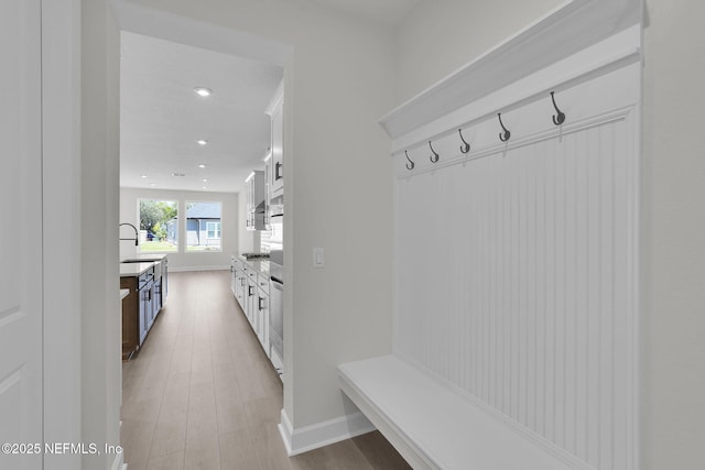 mudroom with a sink, light wood finished floors, recessed lighting, and baseboards