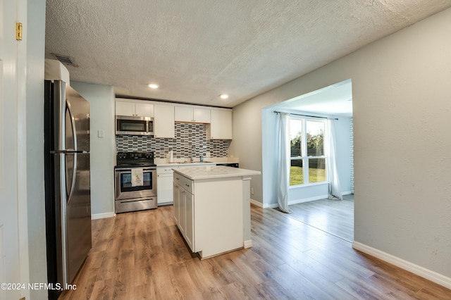 kitchen with light hardwood / wood-style flooring, a textured ceiling, appliances with stainless steel finishes, a kitchen island, and white cabinetry