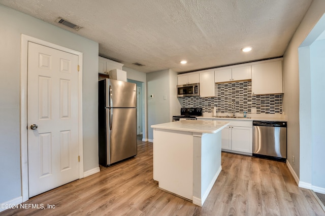 kitchen featuring light wood-type flooring, a textured ceiling, stainless steel appliances, white cabinets, and a center island