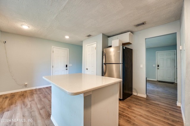 kitchen featuring a center island, stainless steel fridge, a textured ceiling, white cabinets, and light wood-type flooring