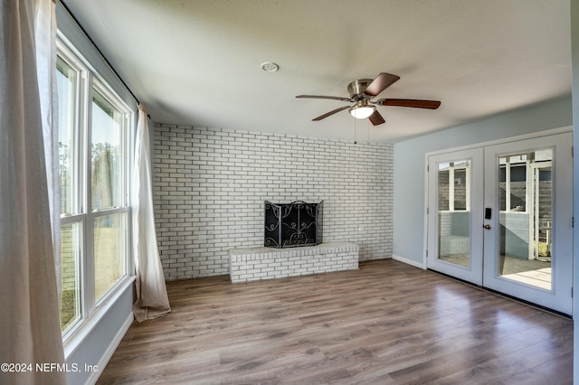 unfurnished living room featuring hardwood / wood-style floors, french doors, a brick fireplace, ceiling fan, and brick wall