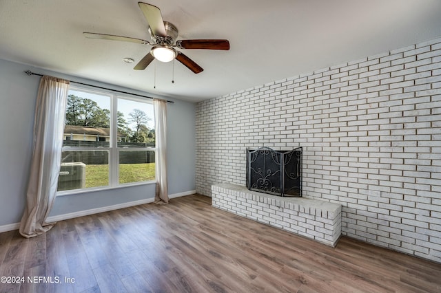 unfurnished living room featuring hardwood / wood-style floors, ceiling fan, brick wall, and a brick fireplace