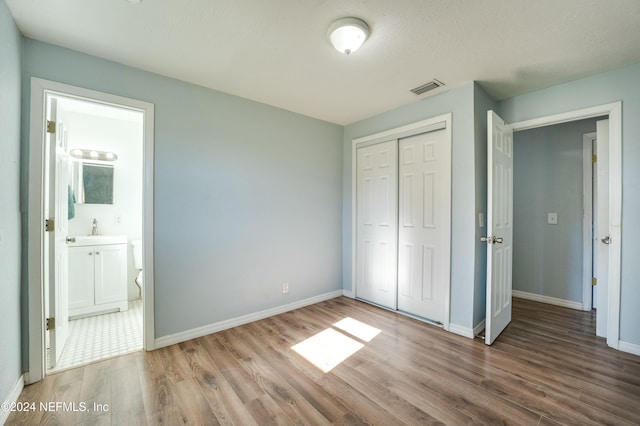 unfurnished bedroom with sink, ensuite bathroom, hardwood / wood-style floors, a textured ceiling, and a closet