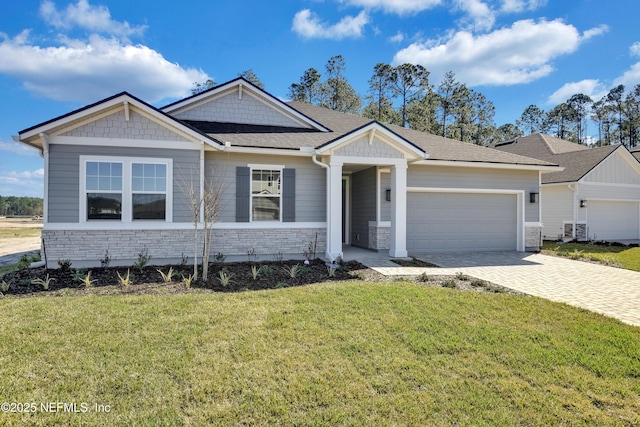 craftsman inspired home featuring decorative driveway, a front yard, stone siding, and an attached garage