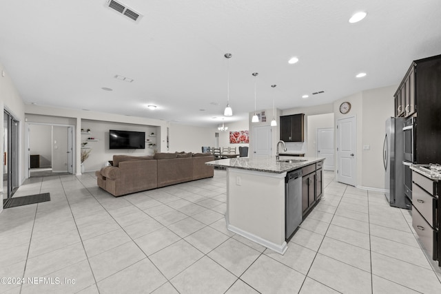 kitchen with light stone countertops, appliances with stainless steel finishes, a center island with sink, and dark brown cabinets