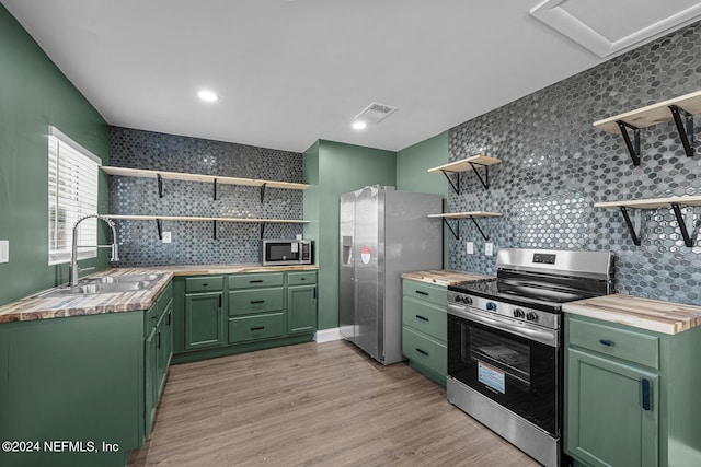 kitchen with sink, green cabinetry, decorative backsplash, butcher block countertops, and stainless steel appliances