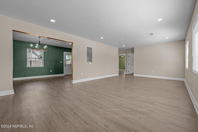 unfurnished living room featuring wood-type flooring, electric panel, and a chandelier