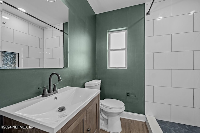 bathroom featuring a tile shower, toilet, vanity, and hardwood / wood-style flooring