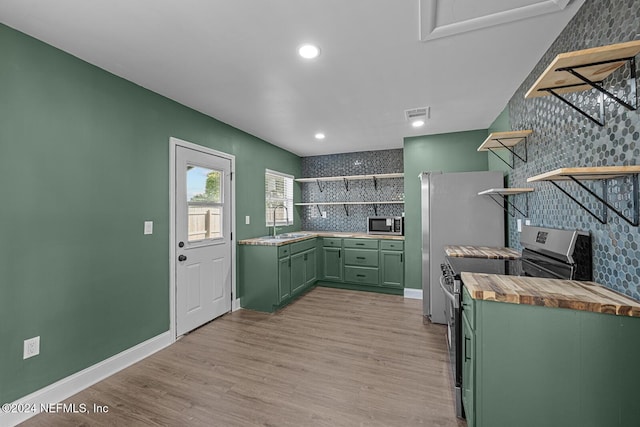 kitchen with wood counters, tasteful backsplash, green cabinets, appliances with stainless steel finishes, and light wood-type flooring